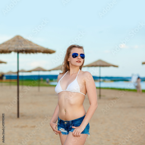 portrait of a girl in a bikini and sunglasses on the beach. Cheerful positive hipster girl on the beach.