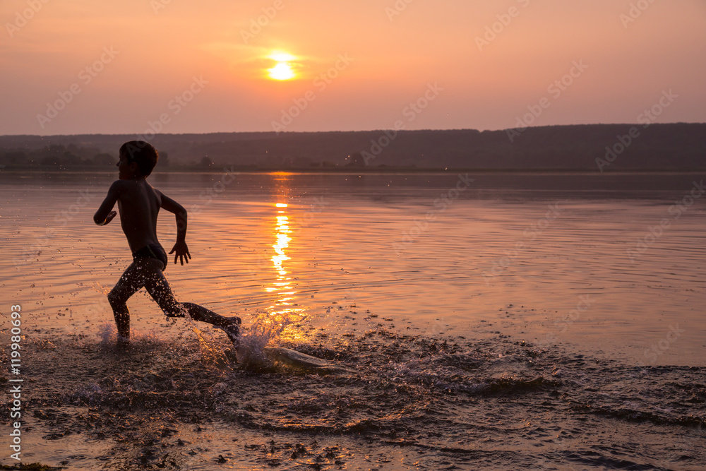 Boy running on river's beach against sunset