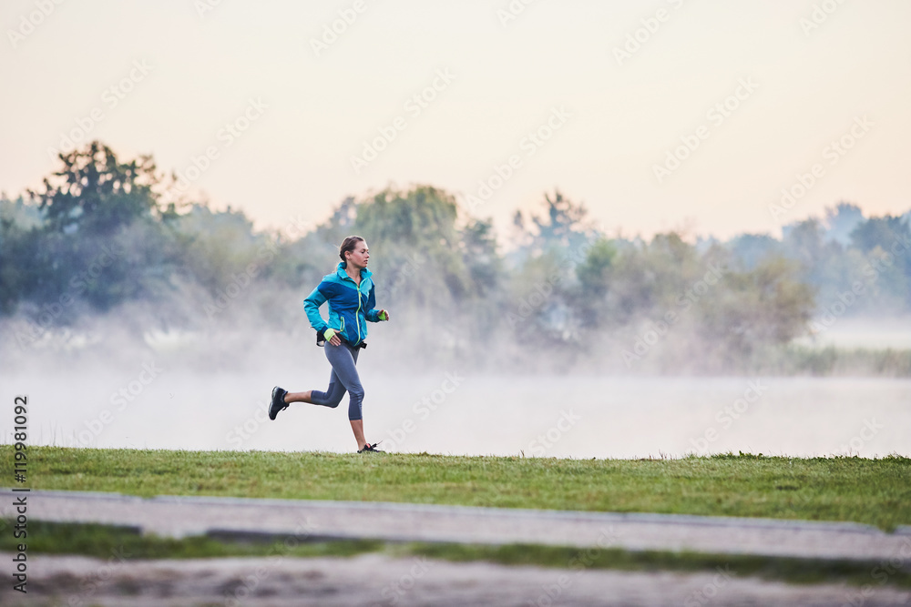 Fit woman running in park during foggy morning