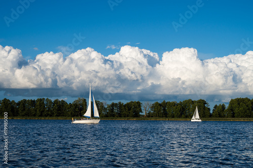 Fototapeta Naklejka Na Ścianę i Meble -  Dwa jachty żaglowe żeglujące po jeziorze, w tle rozbudowujące się chmury Cumulus