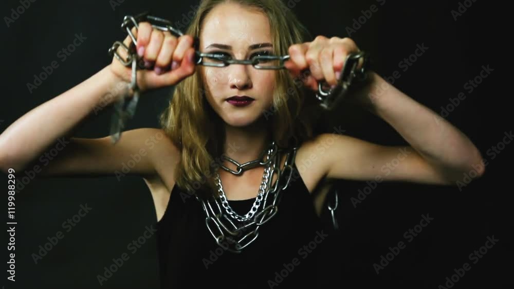 A young woman in a black dress, in a dark room trying to break the metal chain. A young woman in a black dress, in a dark room trying to break the metal chain.
