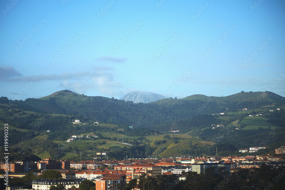 Green hills and snow covered mountain above a quiet seaside town under a blue sunny sky