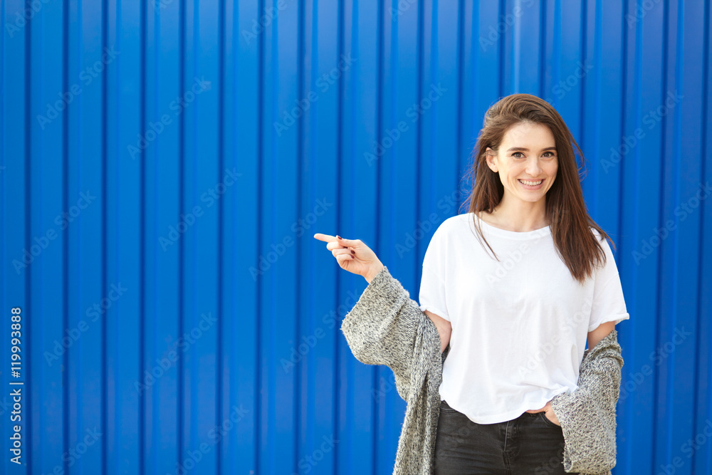 Pretty young woman pointing to copy space. Blue background. Pretty young woman pointing to copy space. Blue background.