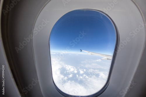 airplane window with wing and cloudy sky behind.
