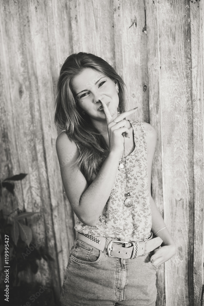 Fototapeta premium Black and white portrait of attractive teenage girl with finger on lips, secret gesture, young pretty woman