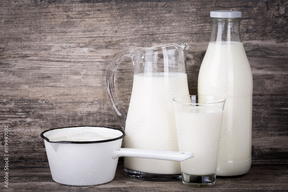 Milch in Krug, Flasche, Stieltopf und Glas auf Holz Hintergrund. Milch in Krug, Flasche, Stieltopf und Glas auf Holz Hintergrund.