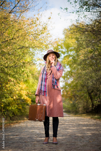 Woman in hat and coat with suitcase on the road