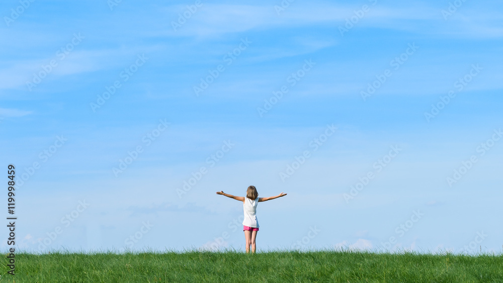 happy little girl standing in a field on blue sky background