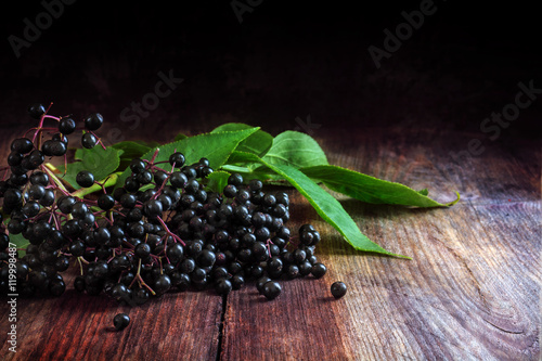 black elderberries (Sambucus nigra) with leaves on a dark wooden background