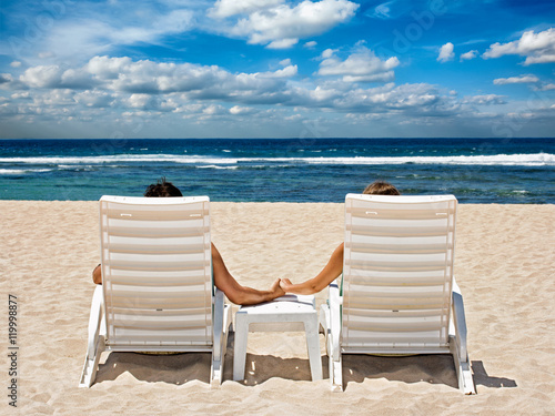 Couple in beach chairs holding hands near ocean