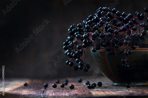 Black elderberries bunch (Sambucus nigra) in an old clay bowl, rustic wood, dark background