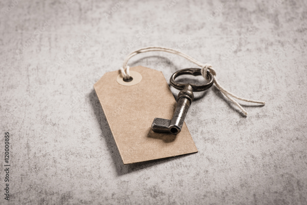 Vintage key with blank paper tag on stone table. Symbol of new home ...