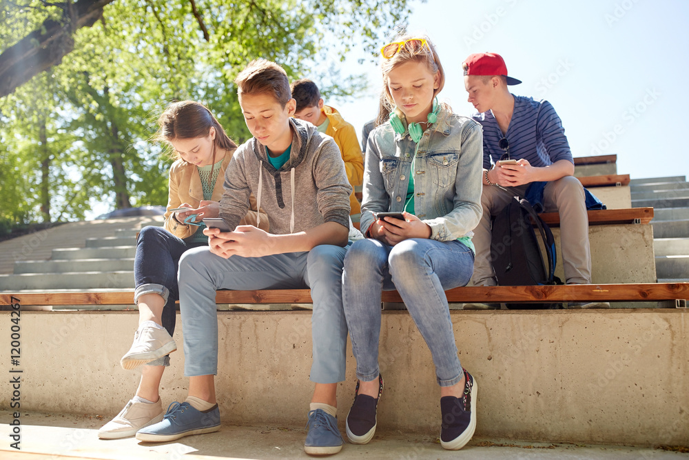 group of teenage friends with smartphones outdoors