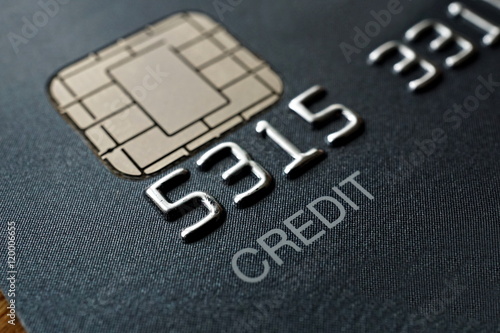 Macro detail of a brand new black and gray luxurious credit card with focus on the caption Credit, metal electronic chip and embossed numbers and letters 