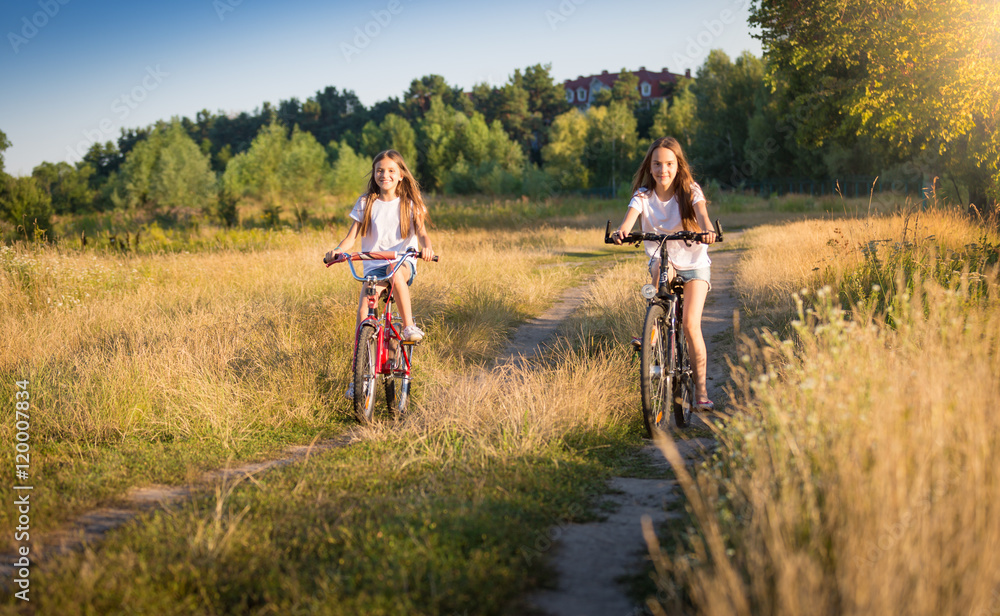 Fototapeta premium Two girls riding bicycles on meadow at sunny day