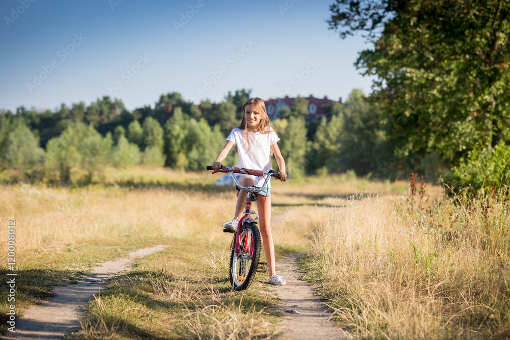 Cheerful girl riding bike in meadow at sunny day
