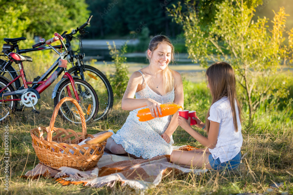 Young mother having picnic by the river with daughter. Mother po Young mother having picnic by the river with daughter. Mother po
