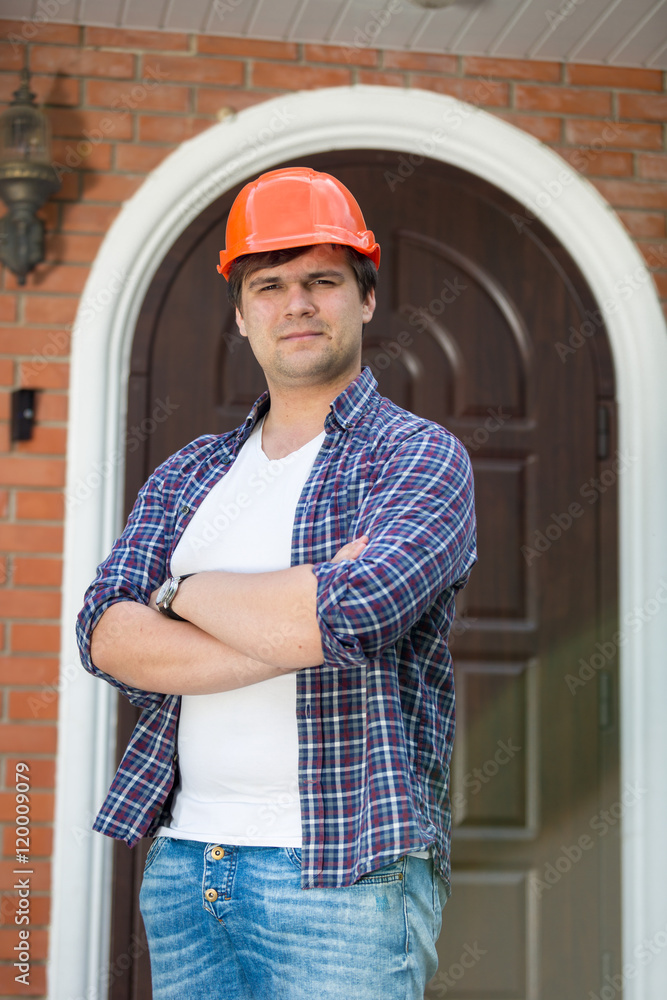Handsome foreman in hardhat posing against new built house