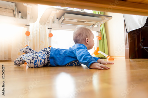 View from under the bed on baby crawling on floor at bedroom