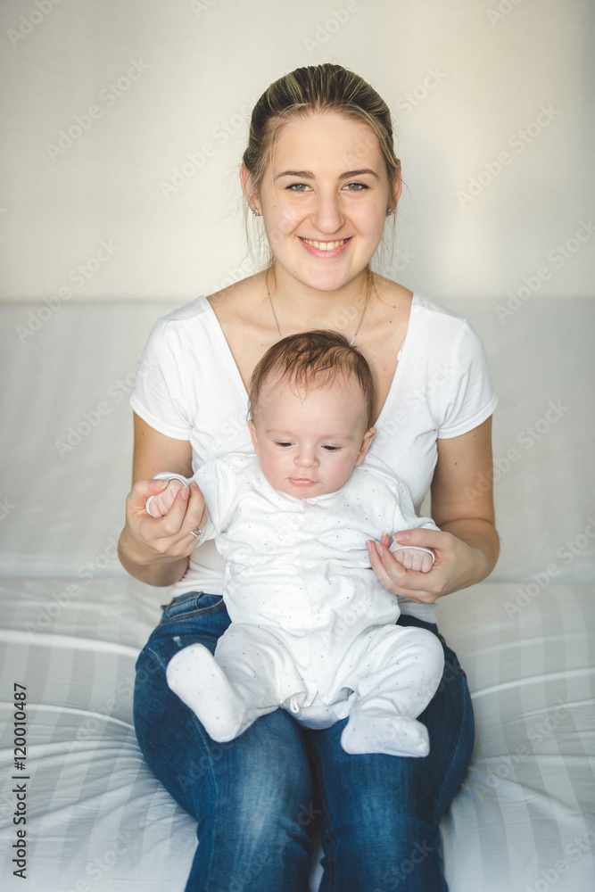 Beautiful smiling mother sitting on bed and holding her baby boy Beautiful smiling mother sitting on bed and holding her baby boy