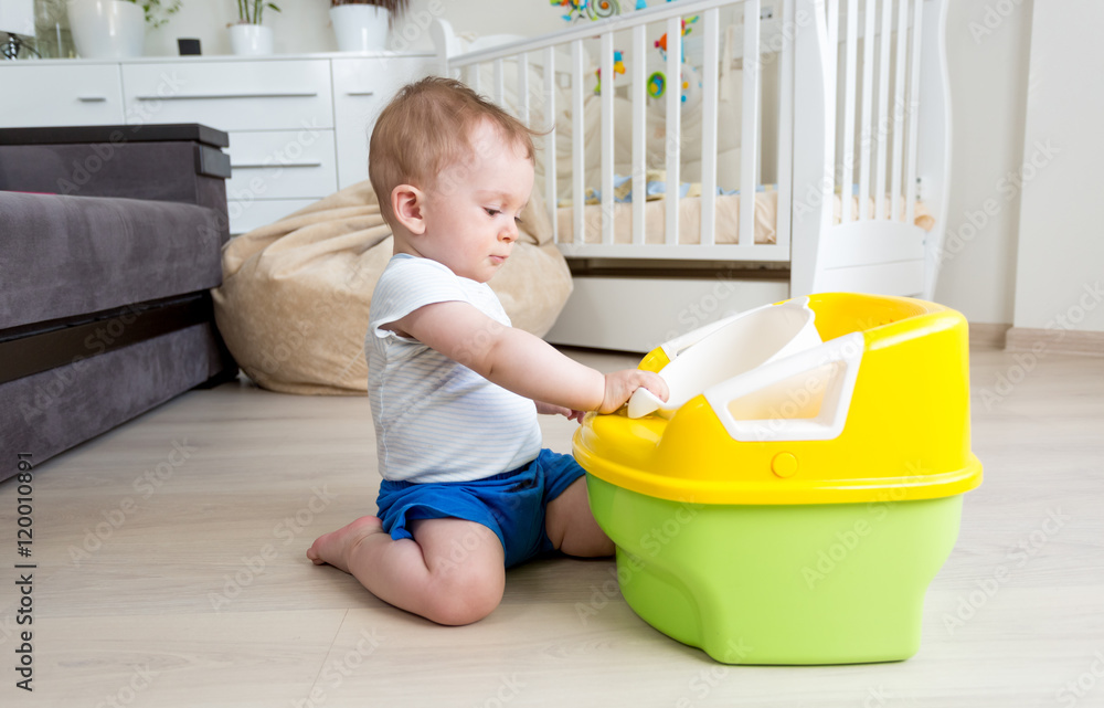 Adorable baby sitting on floor and looking at chamber pot Adorable baby sitting on floor and looking at chamber pot