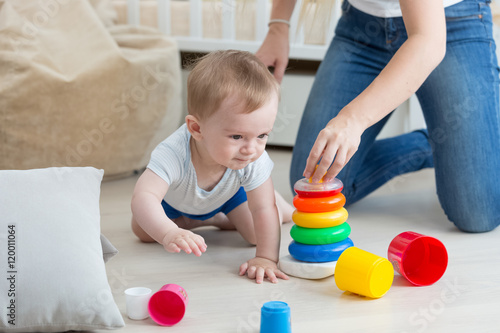 Adorable baby crawling on floor and assembling toy tower with mo