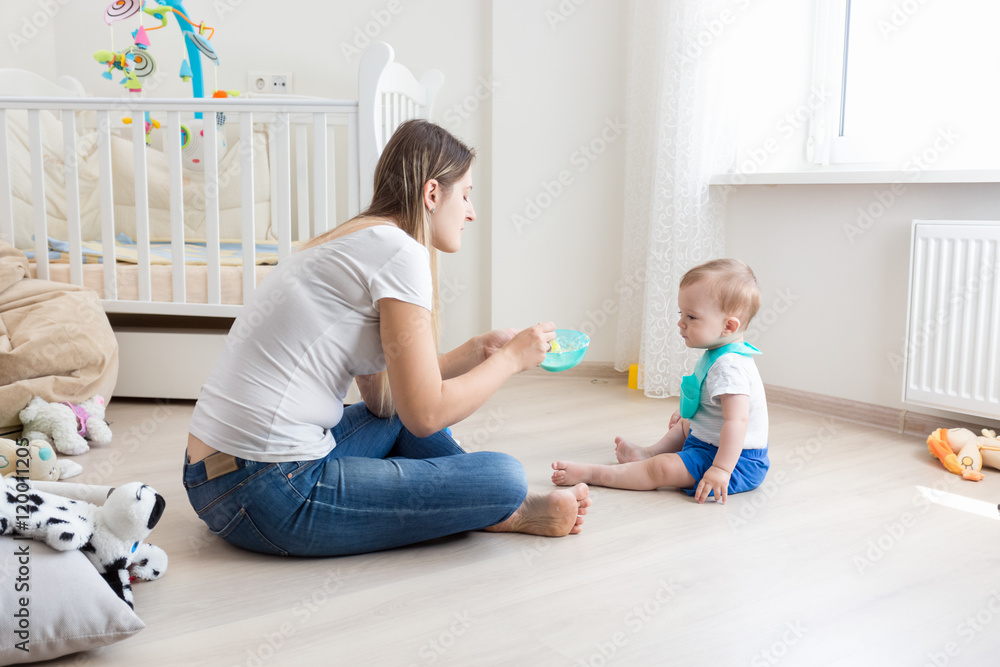 Φωτογραφία Beautiful mother sitting on floor at living room and feeding her