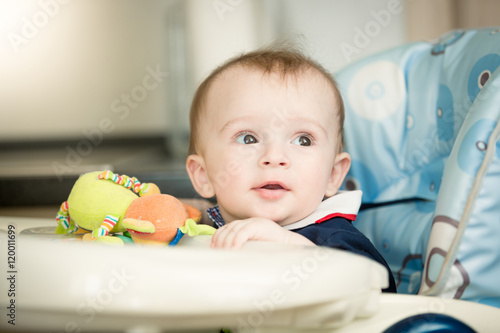 Cute baby boy sitting in child chair with table