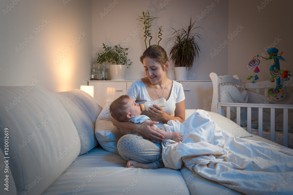 Φωτογραφία Beautiful young mother giving milk to her baby boy in bed at nig