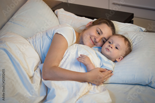 Portrait of happy smiling mother embracing her baby in bed at ni