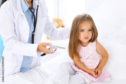 Doctor examining a little girl by stethoscope. Patient turned away from his physician