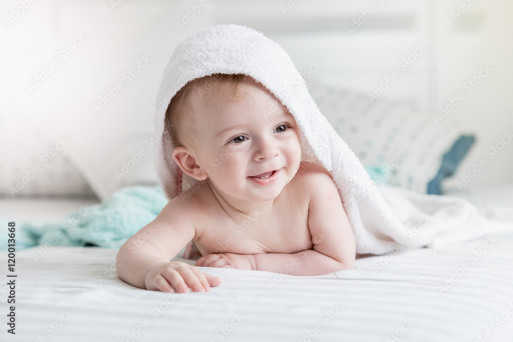 Φωτογραφία Adorable smiling baby in hooded towel ling on bed after having b