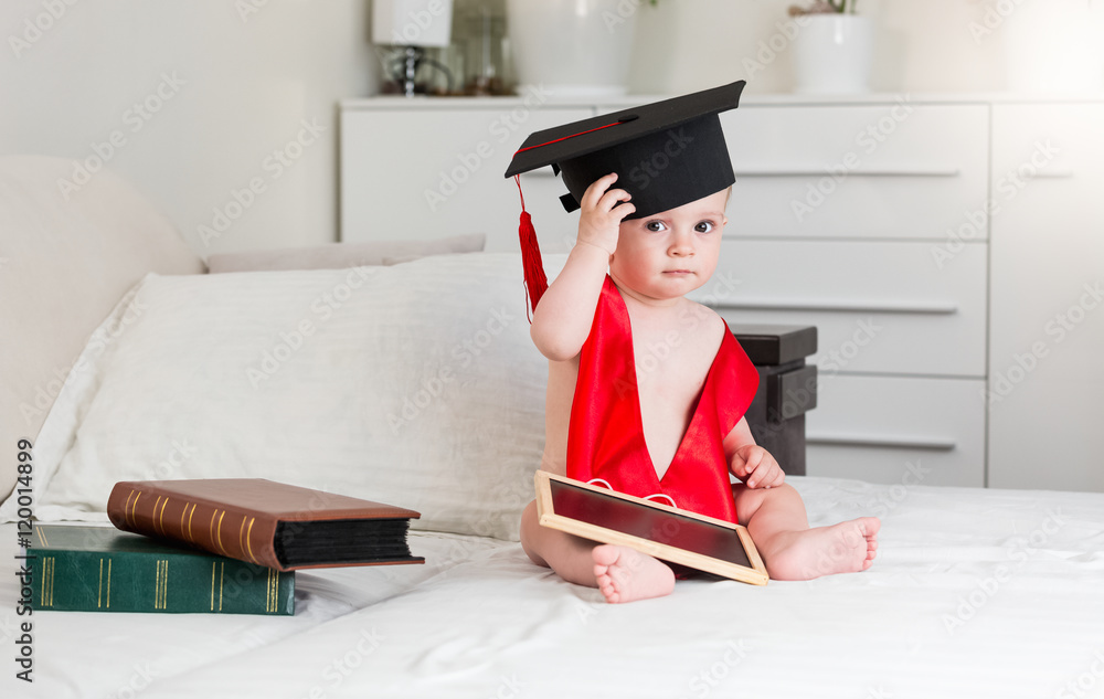 Φωτογραφία Portrait of 10 months old baby boy with books wearing graduation