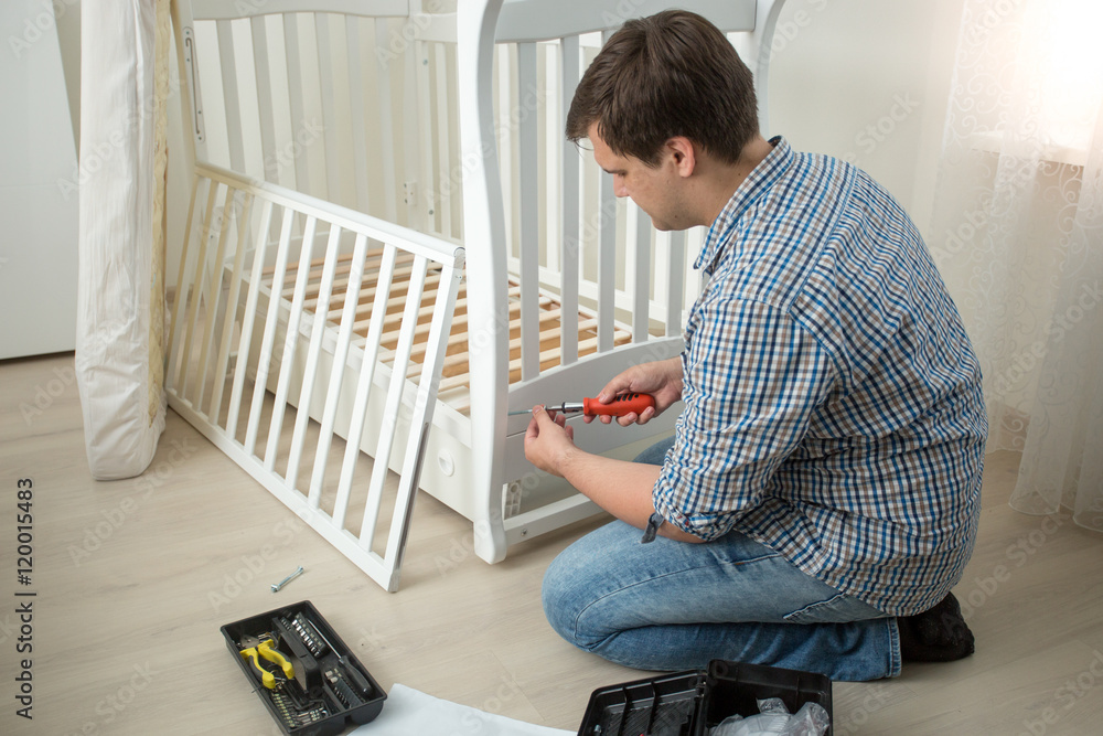 Φωτογραφία Man assembling baby's cot after moving in new house