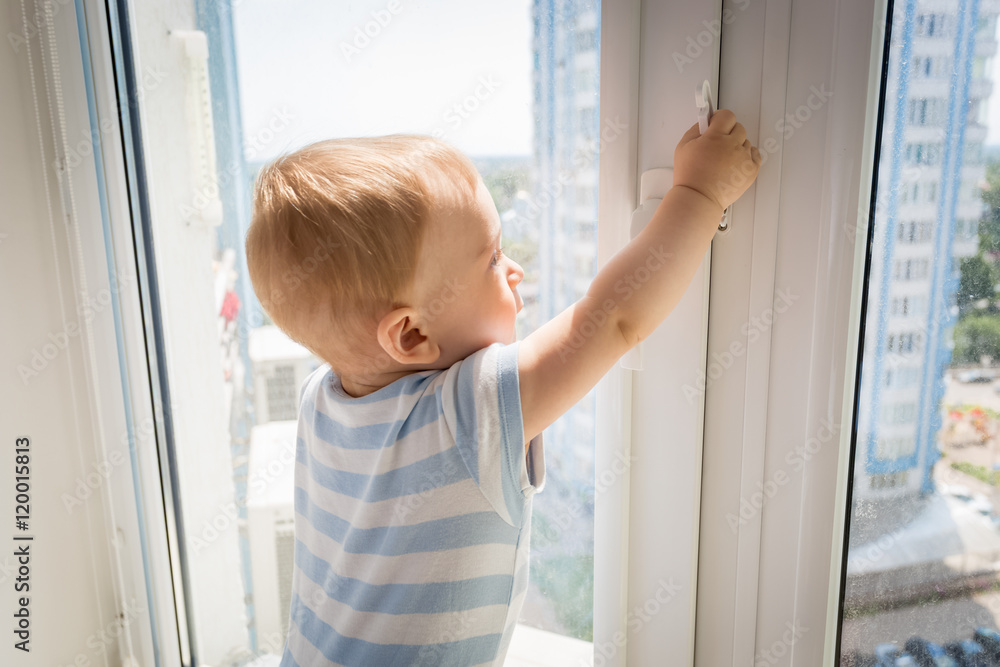 Baby in danger. Little baby trying to open window and pulling by Baby in danger. Little baby trying to open window and pulling by