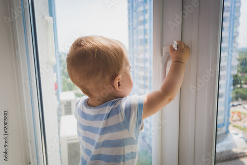 Cute baby boy pulling by the window handle. Concept of child in