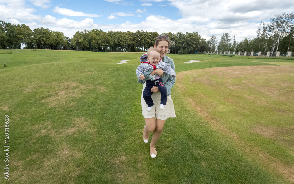 Cheerful mother holding her baby boy and running on grass at par Cheerful mother holding her baby boy and running on grass at par