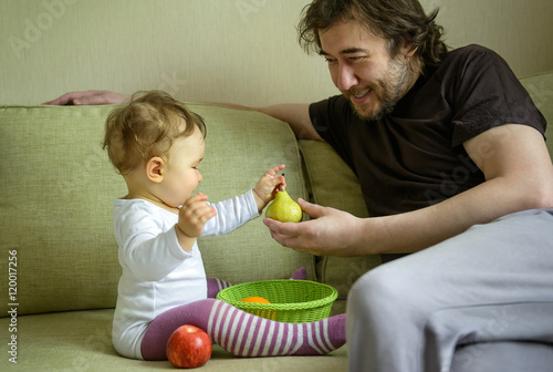 Cute baby girl plays with fruits with her father at home photo