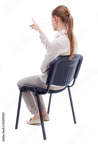 back view of young beautiful woman sitting on chair and pointing. Skinny girl in white denim suit sidit thoughtfully in his chair and points. photo