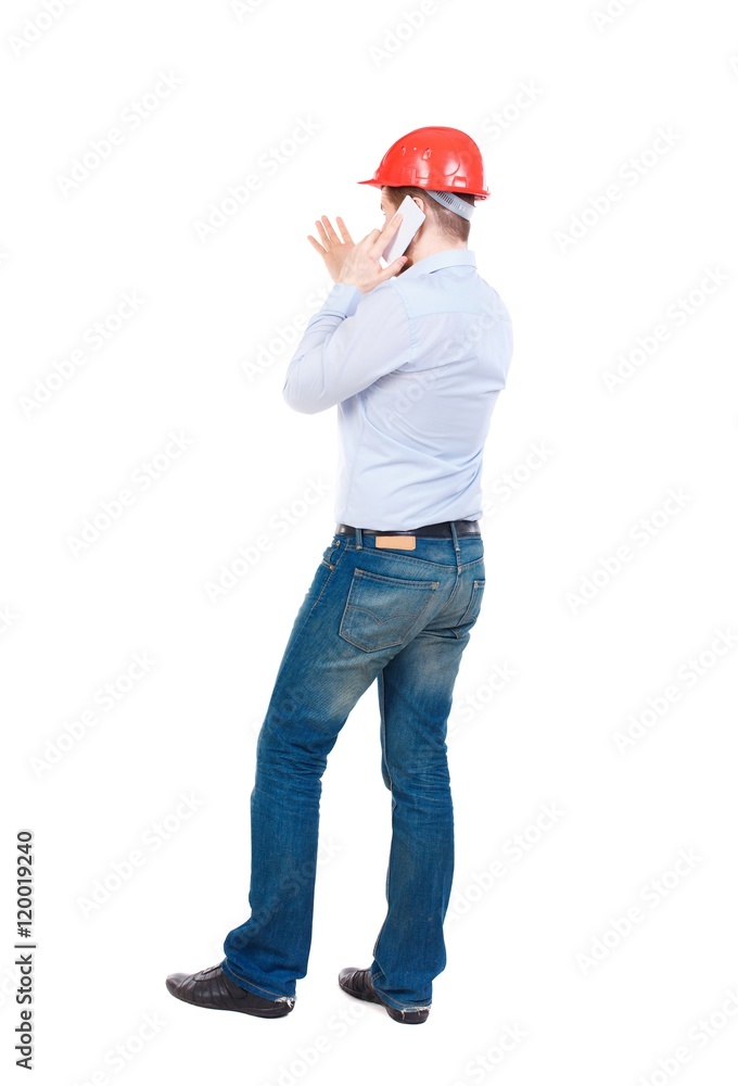 Backview of business man in construction helmet stands and enjoys tablet or using a mobile phone. businessman in a white shirt and a construction helmet talking on the phone and gesticulates. Backview of business man in construction helmet stands and enjoys tablet or using a mobile phone. businessman in a white shirt and a construction helmet talking on the phone and gesticulates.