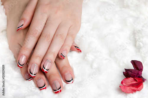 French manicure - beautiful manicured female hands with red black and white manicure with rhinestones on a soft white coat