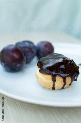 Sweet profiteroles with cream and chocolate glaze and plums on a