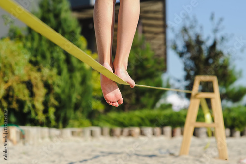 Girl walking on the sling. Child balancing on slackline at a beach. Shadow of a human figures on the sand. Girl is balancing on one leg. photo