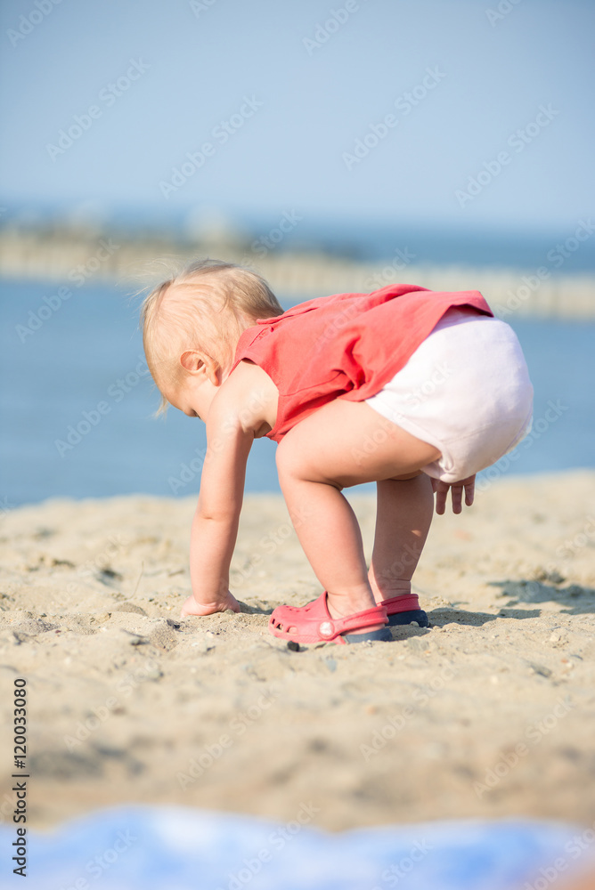Baby playing on the sandy beach near the sea. Cute little girl in red ...