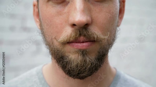 Close up man 's face with a beard and mustache, white brick wall background, zoom out