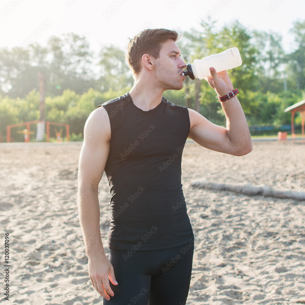 Training Outdoors. Athletic fit man drinking water after running workout at beach. Training Outdoors. Athletic fit man drinking water after running workout at beach.