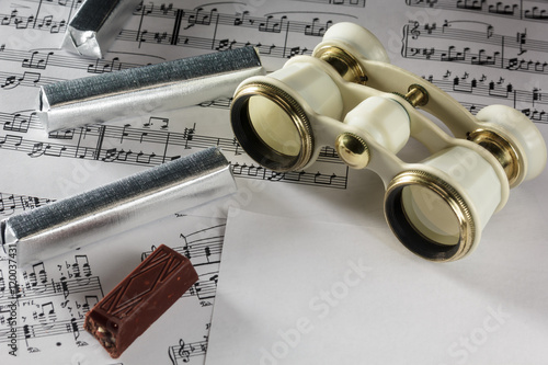 Antique opera glasses rest on a musical notes.