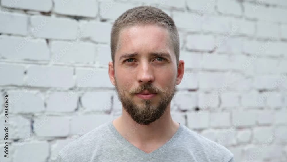 Serious man with a beard and mustache looking at the camera, white brick wall background Serious man with a beard and mustache looking at the camera, white brick wall background