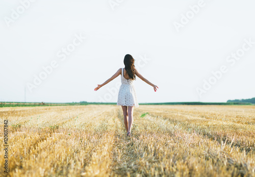 Portrait of a beautiful brunette woman in wheat field with her arms outstretched.