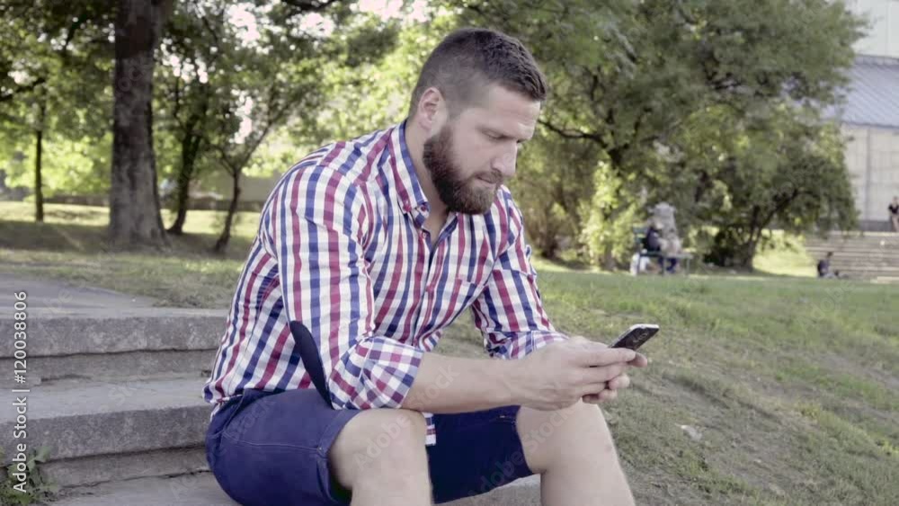 Man browsing smartphone. He is sitting on stairs in the park. He is dressed in blue shorts and checkered shirt. He has beard. Slider and pan shot.
Man browsing smartphone. He is sitting on stairs in the park. He is dressed in blue shorts and checkered shirt. He has beard. Slider and pan shot.